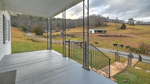 A porch with a view of a rural landscape, including a road, a fenced area with cows, and a small building. - Walter & Mae's Farmhouse: Charming accomodations with gorgeous mountain views (Elizabethton)