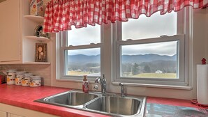 A kitchen with a red countertop, double sink, and a view of mountains through two windows. - Walter & Mae's Farmhouse: Charming accomodations with gorgeous mountain views (Elizabethton)