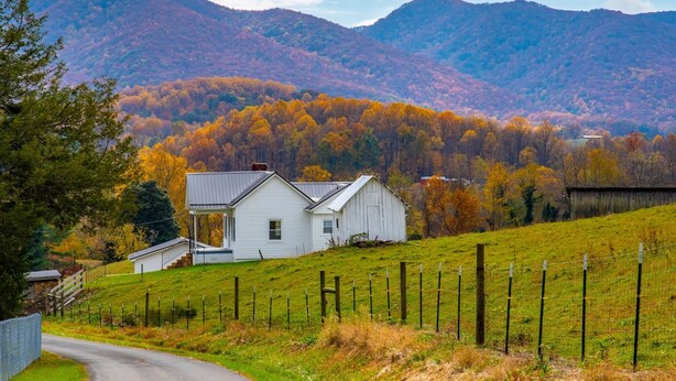 A white house with a porch, a fenced yard, and a mountain backdrop. - Walter & Mae's Farmhouse: Charming accomodations with gorgeous mountain views (Elizabethton)
