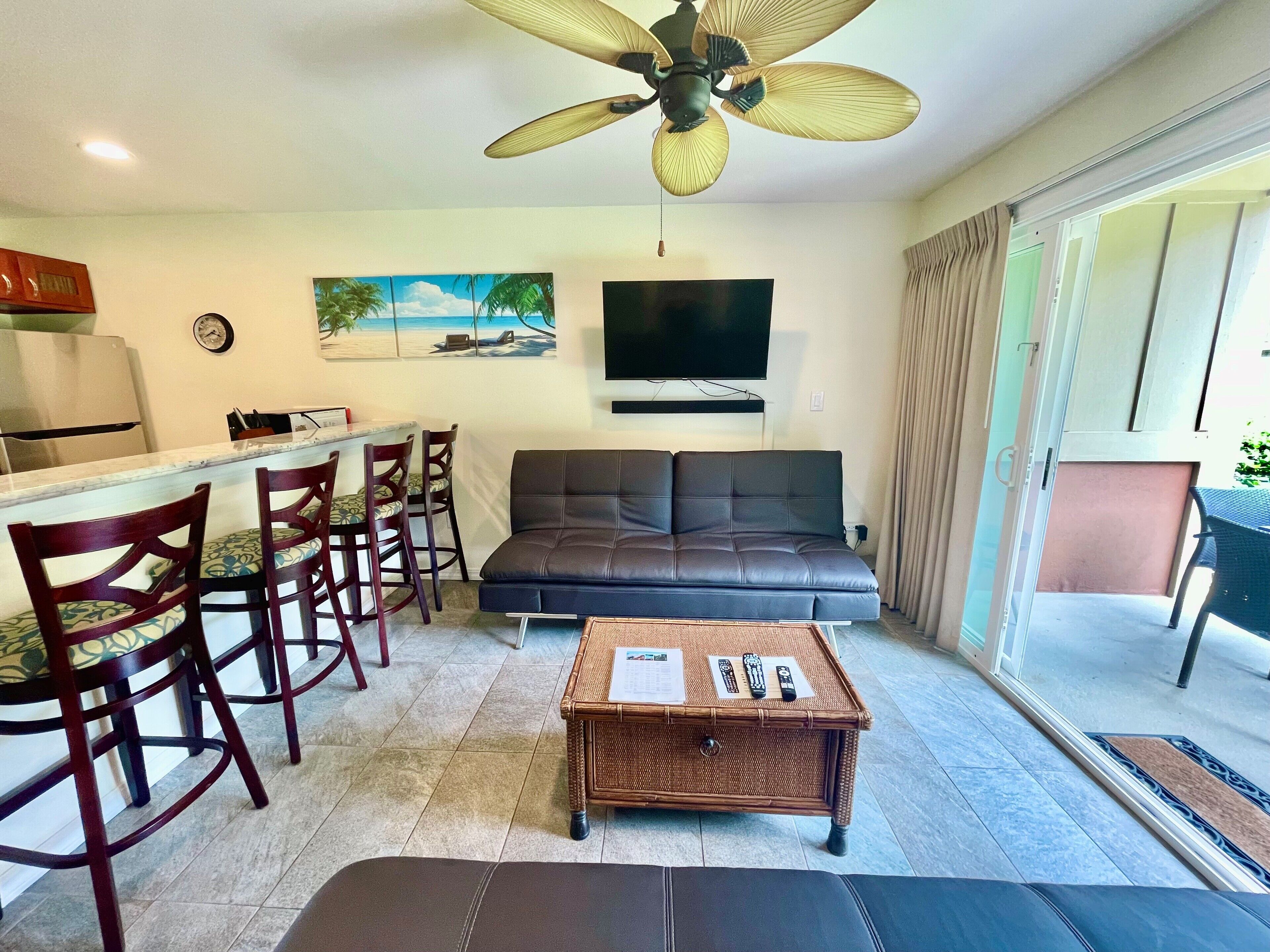 Un espace de vie comprenant un canapé, une table à manger avec des chaises, un téléviseur et un ventilateur de plafond.