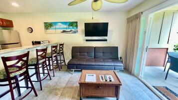 Un espace de vie comprenant un canapé, une table à manger avec des chaises, un téléviseur et un ventilateur de plafond.