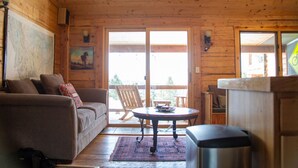 Interno di una baita in legno con divano, tavolo da pranzo e vista attraverso le vetrate.