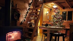 Un accogliente interno di una baita con una scala in legno, un camino, una zona pranzo e un albero di Natale decorato.