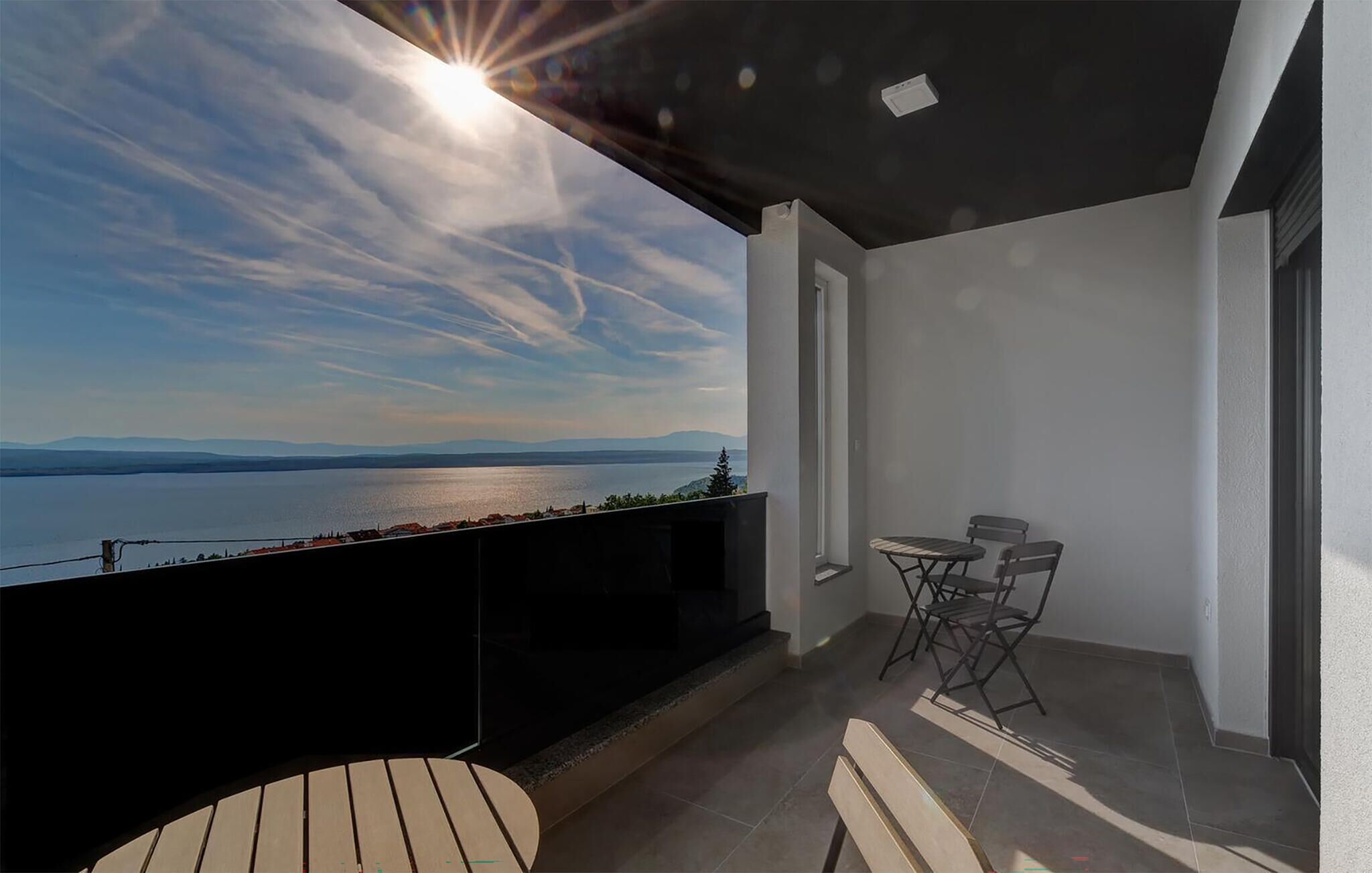 Ein Balkon mit Seeblick und Bergblick, ein kleiner Tisch mit Stühlen und die Sonne, die durch die Wolken scheint.