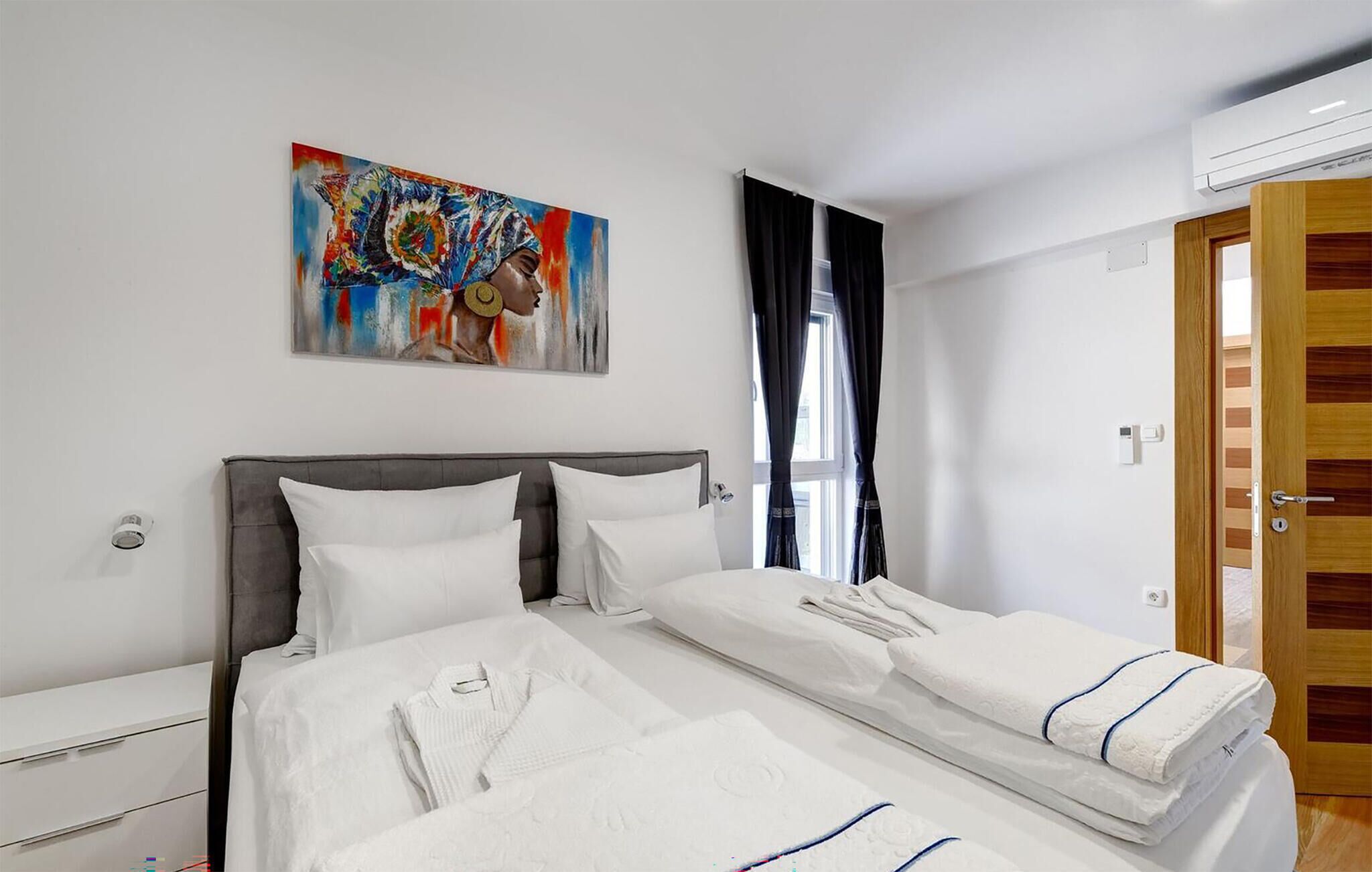 Habitació d'hotel amb un llit, un quadre a la paret, una finestra amb cortines i una porta.