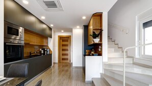 A modern kitchen with built-in appliances, a dining area with a marble table, and a staircase leading to an upper floor.