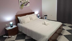 Een net opgemaakt bed met witte lakens, een bedlampje en een luchtverkoeler aan de muur.