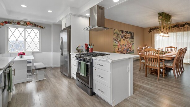 Una cocina moderna con armarios blancos, estufa de acero inoxidable y una zona de comedor con sillas y mesa de madera.
