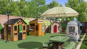 Zona infantil con casitas de juego, una mesa de picnic y una sombrilla.