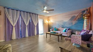 Una sala de estar con ventilador de techo, dos sofás, una mesa de centro y un mural de un castillo en la pared.