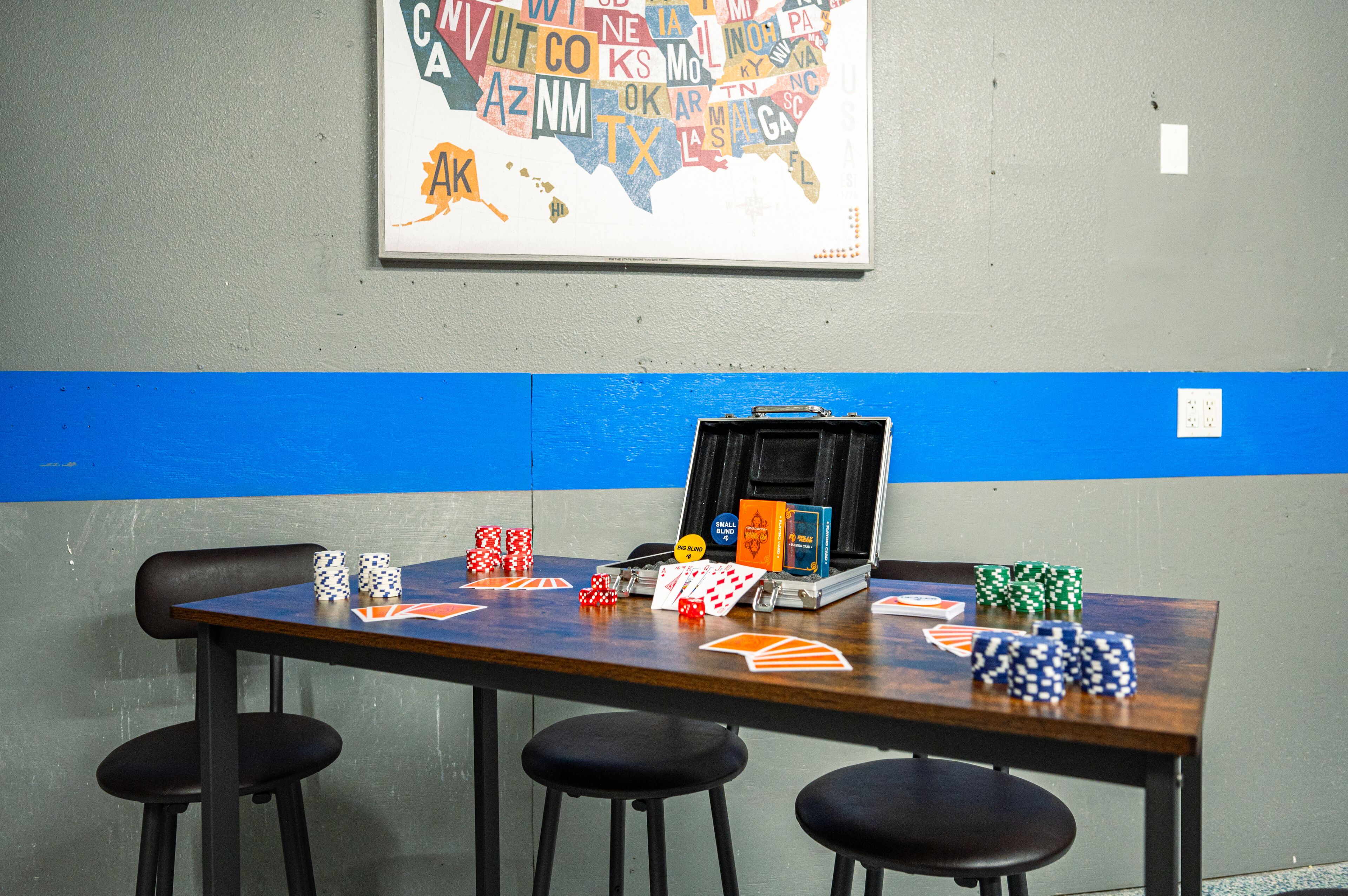 Una mesa de póker con fichas y cartas, un maletín y un mapa de Estados Unidos en la pared.