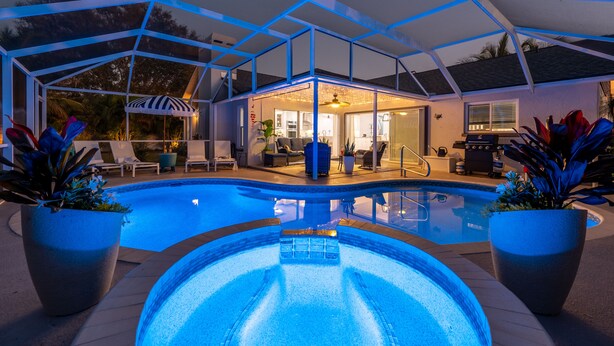 Une piscine entourée de parois en verre, avec des chaises longues et des plantes en pot.