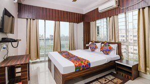 A hotel room with a bed, bedside tables, a desk, a ceiling fan, and a window with curtains. - Fabhotel White House I (Kolkata)
