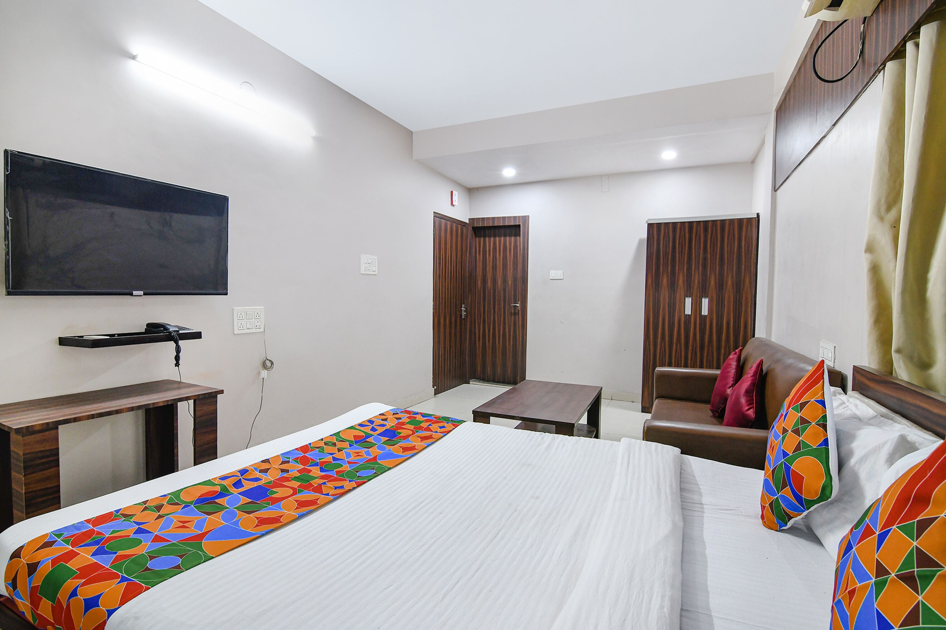 A hotel room with a bed, a desk, a TV, a wardrobe, and a small table.