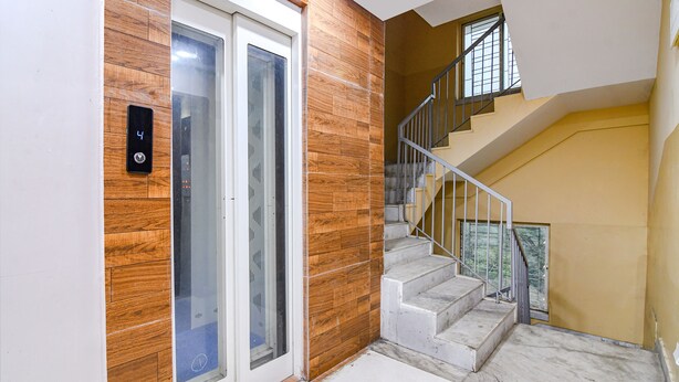A modern interior with a wooden panel wall, a glass door elevator, and a marble staircase. - Fabhotel White House I (Kolkata)