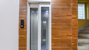 A modern elevator with a control panel, adjacent to a staircase with wooden paneling. - Fabhotel White House I (Kolkata)
