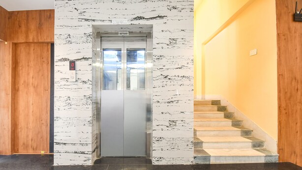 Een lift met een marmeren wand, een houten deur en een trap met stenen treden.