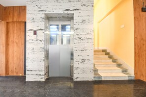 An elevator with a marble wall, a wooden door, and a staircase with stone steps. - Fabhotel Prime The Golden Plaza (Rampurhat)