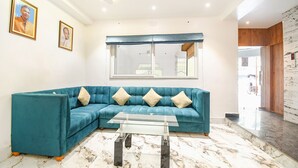 Een woonkamer met een blauwgroene bank, een glazen salontafel en een groot raam met uitzicht.