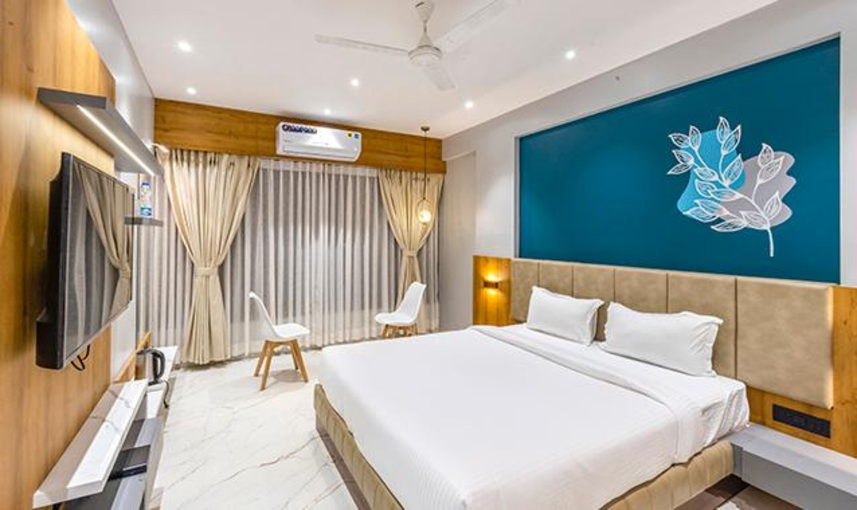 A modern hotel room with a large bed, a flat-screen TV, a desk, and a decorative wall piece.