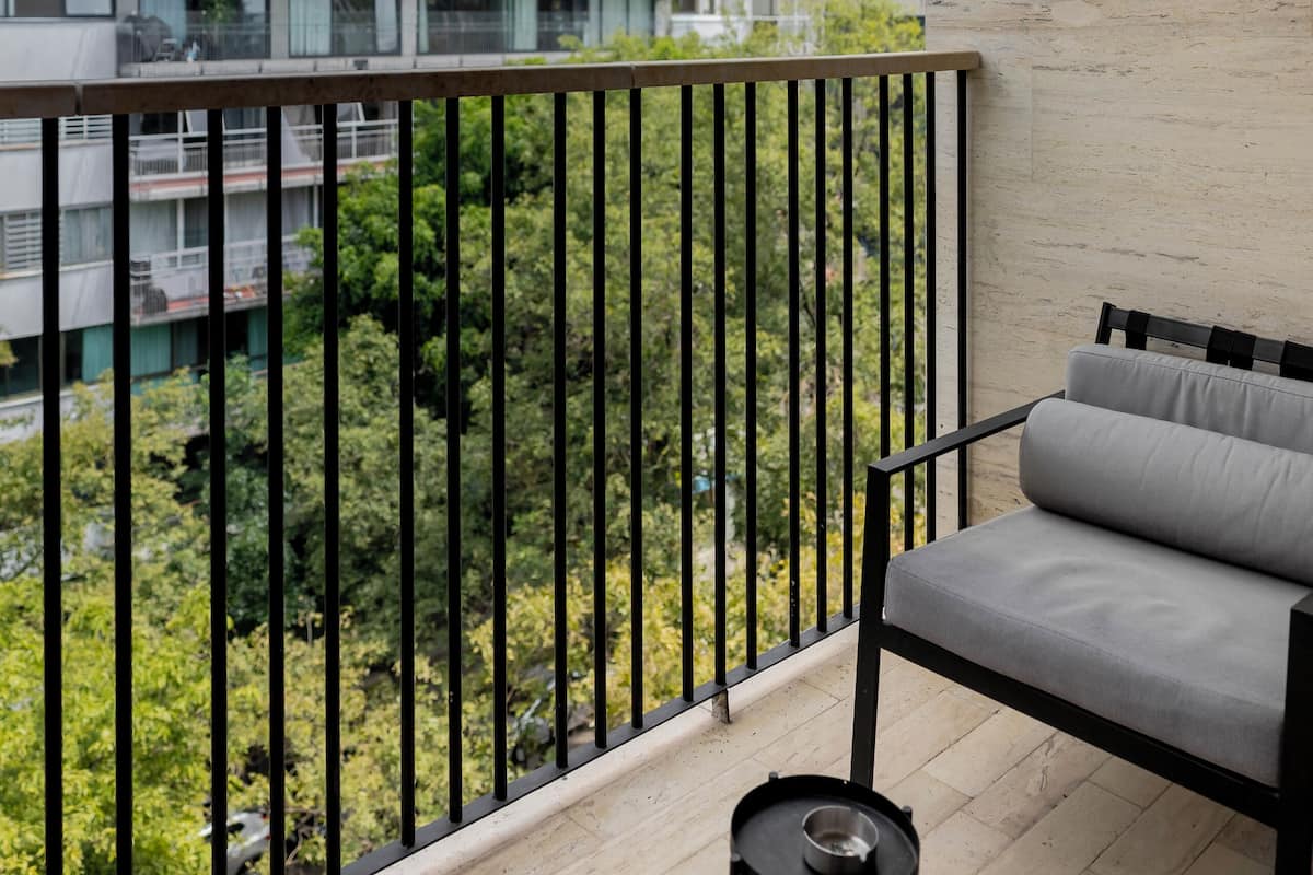A balcony with a grey sofa, a small round table with a bowl and a container, and a view of a multi-story building with balconies.
