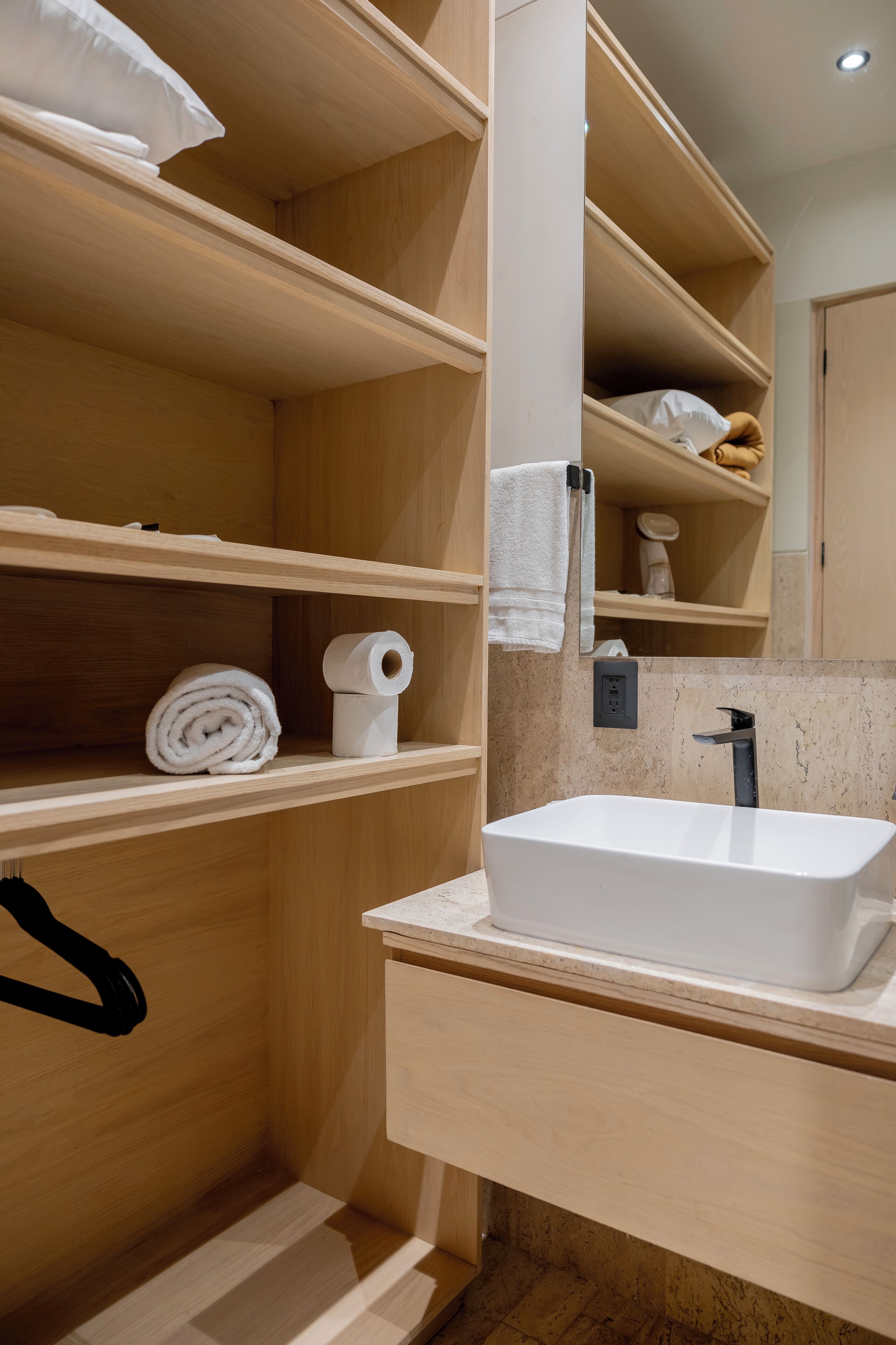 Une salle de bain en bois avec un lavabo blanc, des étagères avec des serviettes et un porte-serviettes.