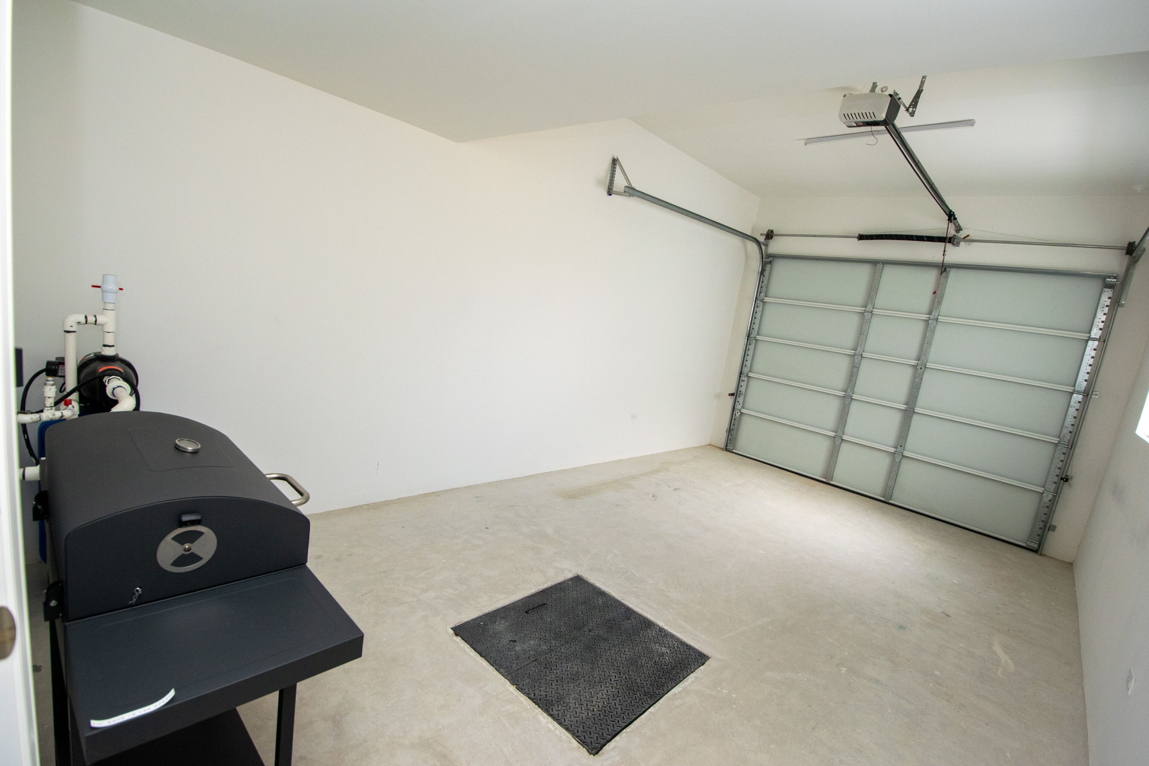 A garage with a ceiling-mounted projector, a garage door, and a black grill on a table.