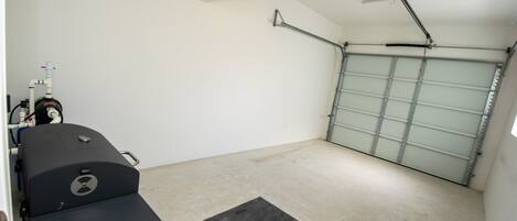 A garage with a ceiling-mounted projector, a garage door, and a black grill on a table.