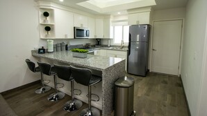 Una cocina moderna con armarios blancos, encimera de granito, refrigerador de acero inoxidable y tres taburetes de bar.