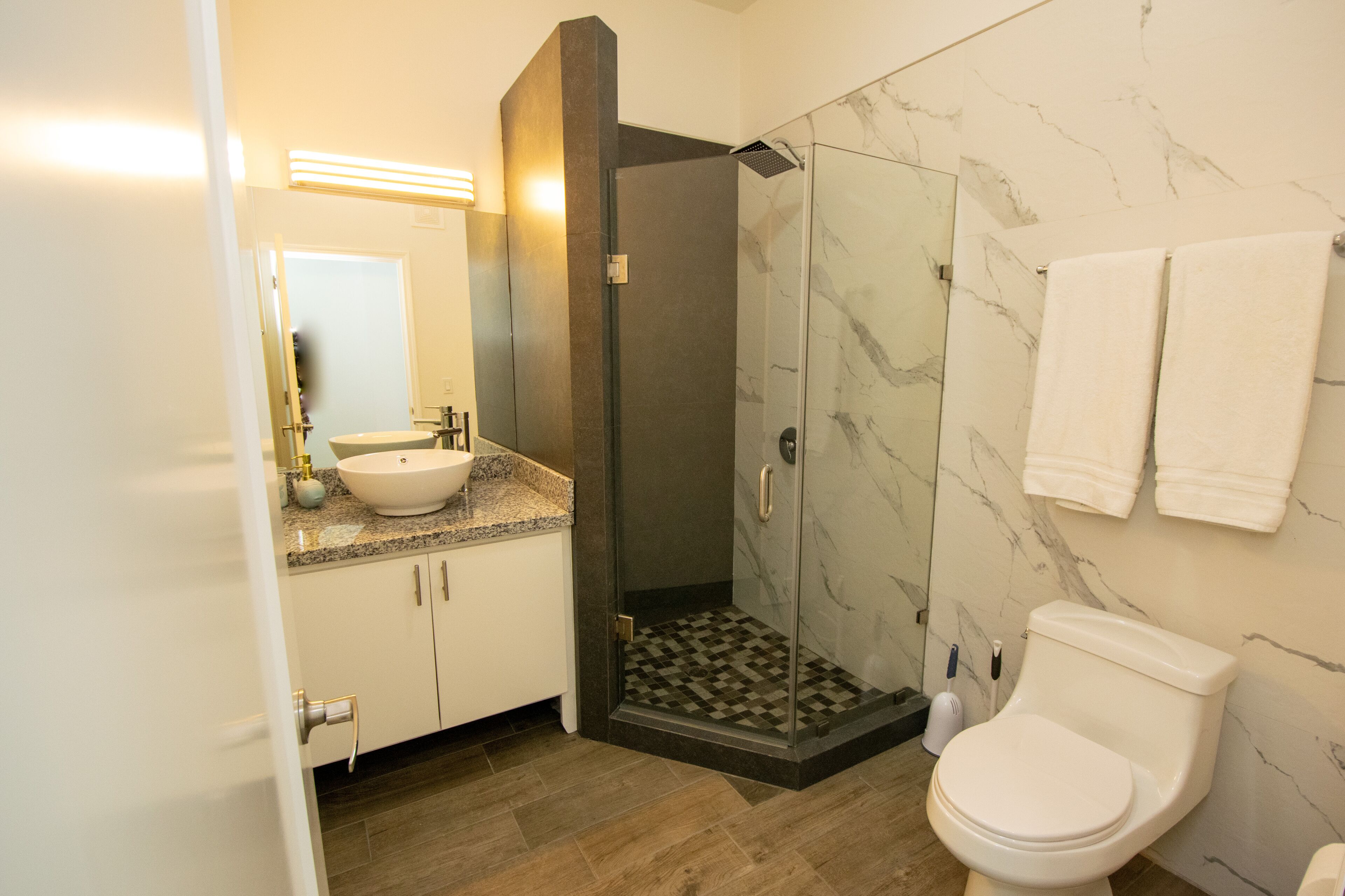 Een badkamer met een witte wastafel, een douche met glazen wanden, een toilet en marmeren wanden.