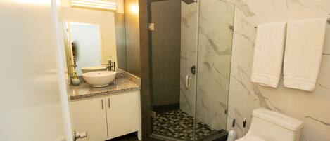 Een badkamer met een witte wastafel, een douche met glazen wanden, een toilet en marmeren wanden.