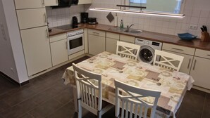 A compact kitchen with white cabinets, a built-in oven, a washing machine, and a table with a patterned tablecloth.
