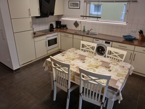Una cocina compacta con armarios blancos, horno empotrado, lavadora y una mesa con mantel estampado.