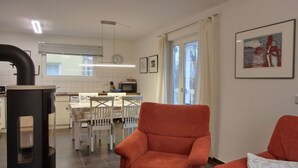 A modern living room with a fireplace, a dining area with a table and chairs, and a kitchen in the background.