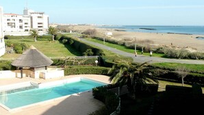 Un complexe hôtelier doté d’une piscine, offrant une vue sur la plage et comprenant un bâtiment à toit de chaume.