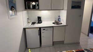 Une cuisine compacte avec des meubles blancs, un four à micro-ondes, une machine à café et un lave-vaisselle.