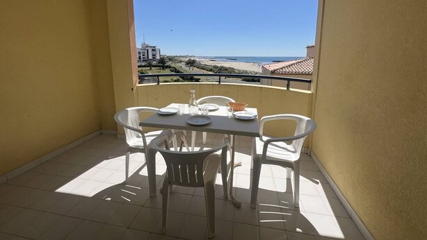 Un balcon avec une table dressée pour deux personnes, des chaises et une vue sur la plage et l’océan.