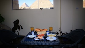 Una mesa de desayuno con alimentos, dos vasos de zumo de naranja y vistas a las pirámides a través de una ventana.