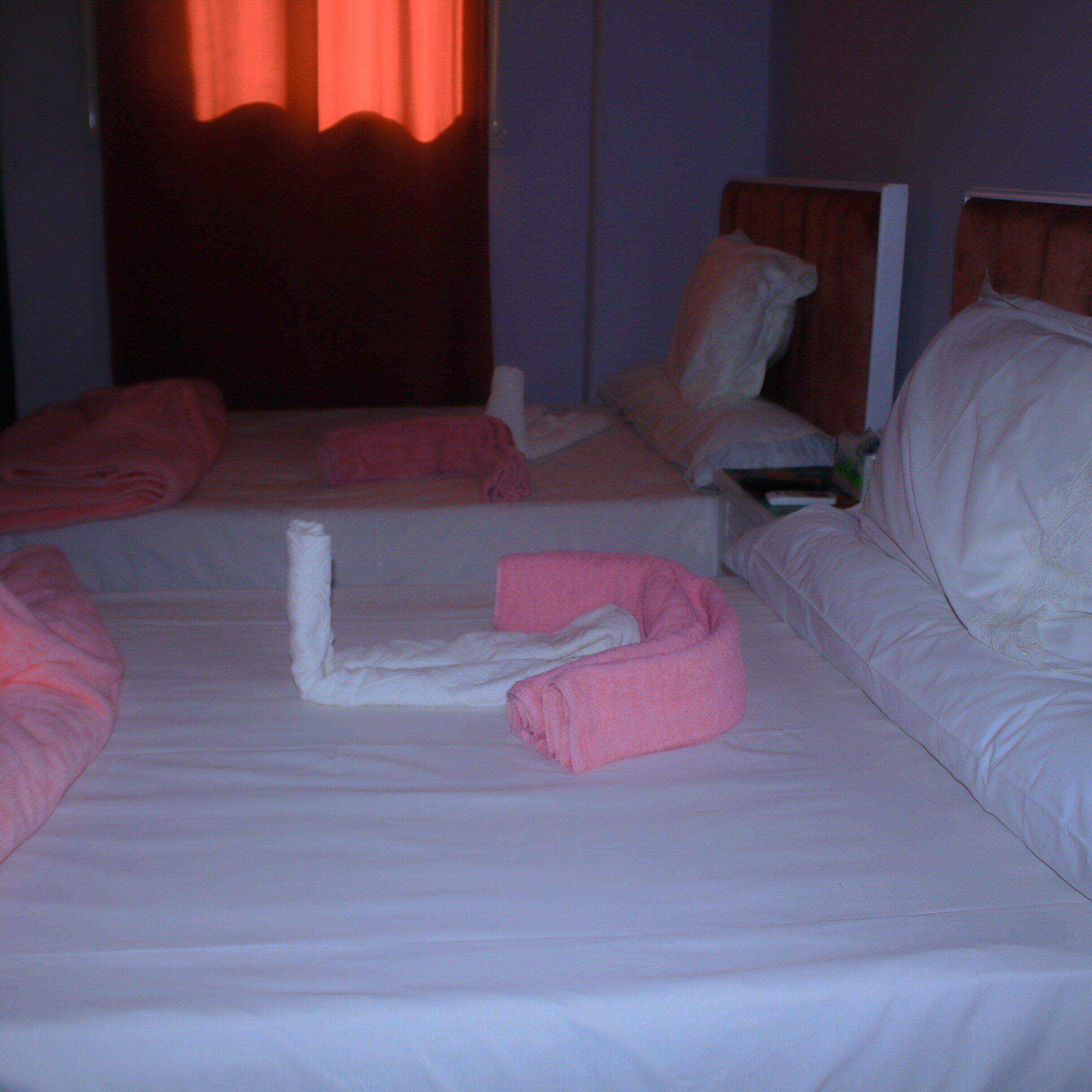 A hotel room with two beds, each with white linens and pink towels.
