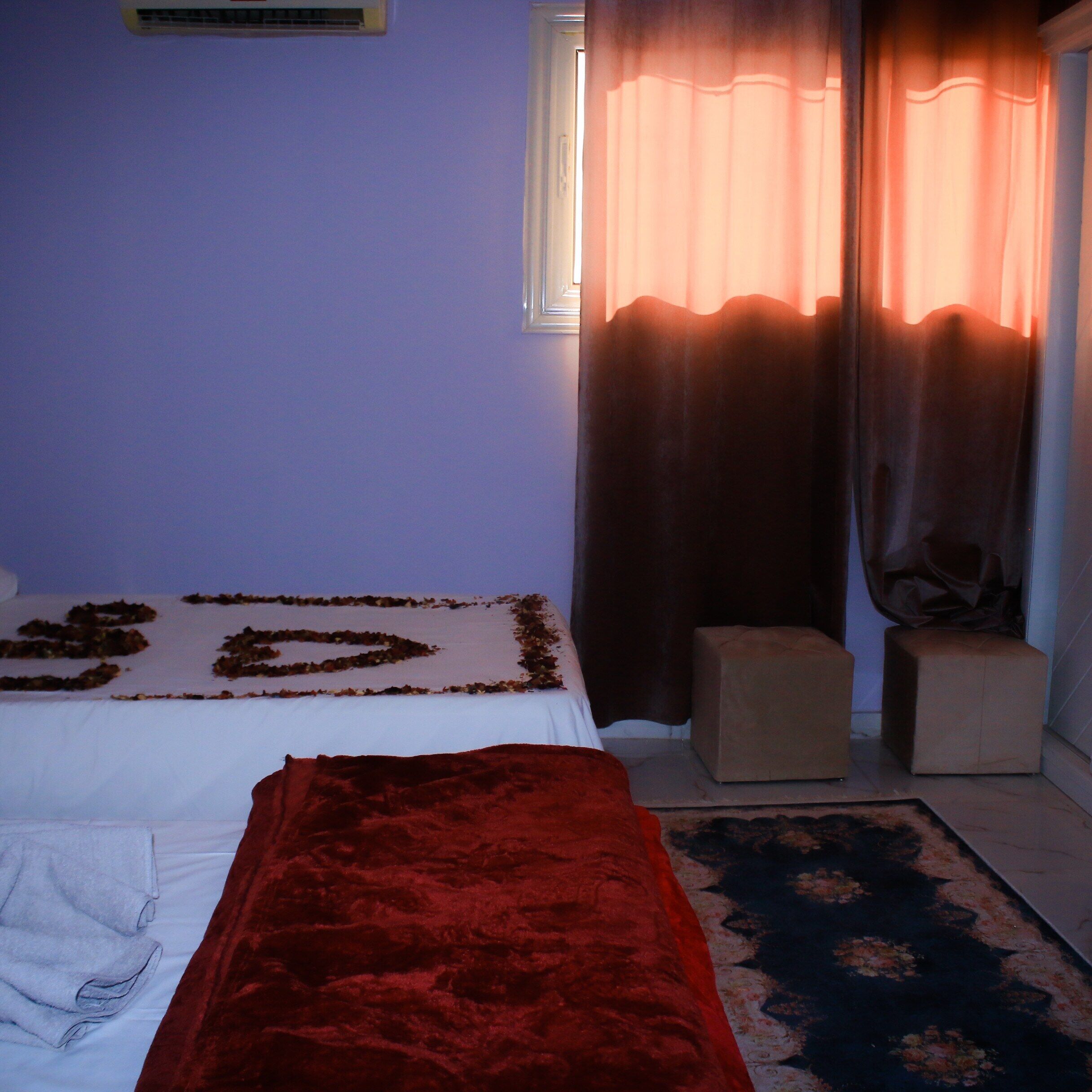 Une chambre à coucher avec un lit, un plaid rouge, un petit tabouret et un tapis à motifs.