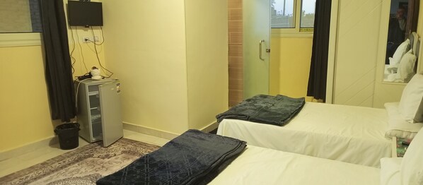 A hotel room with two beds, a desk, a television, and a window.