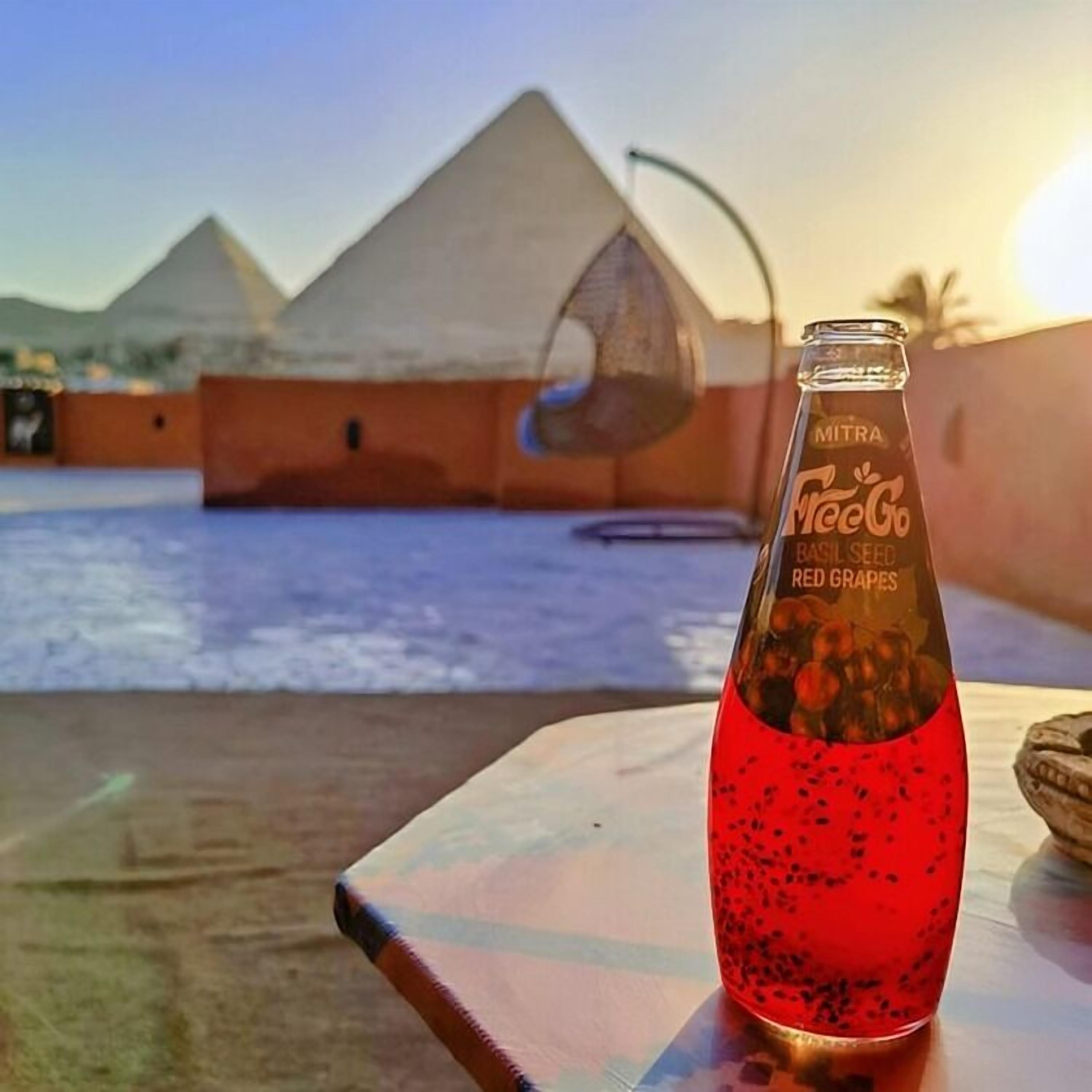 Una botella de bebida de uva roja sobre una mesa, con vistas a las pirámides al fondo.