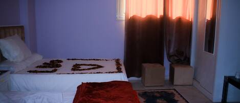 Ein Schlafzimmer mit einem Bett, einer roten Tagesdecke, einem kleinen Hocker und einem gemusterten Teppich.