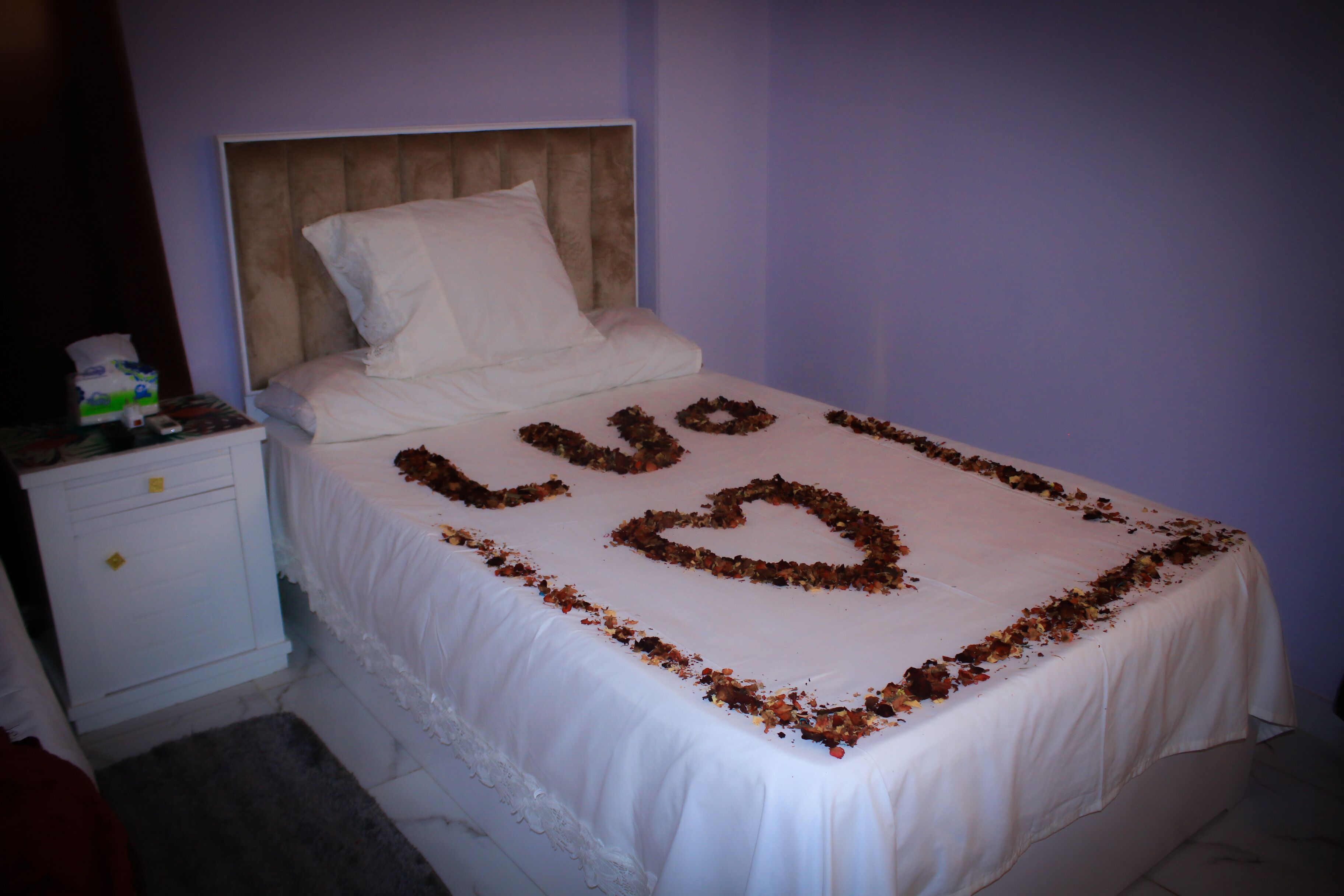 A bed with a white bedspread and a heart-shaped decoration made of dried flowers.