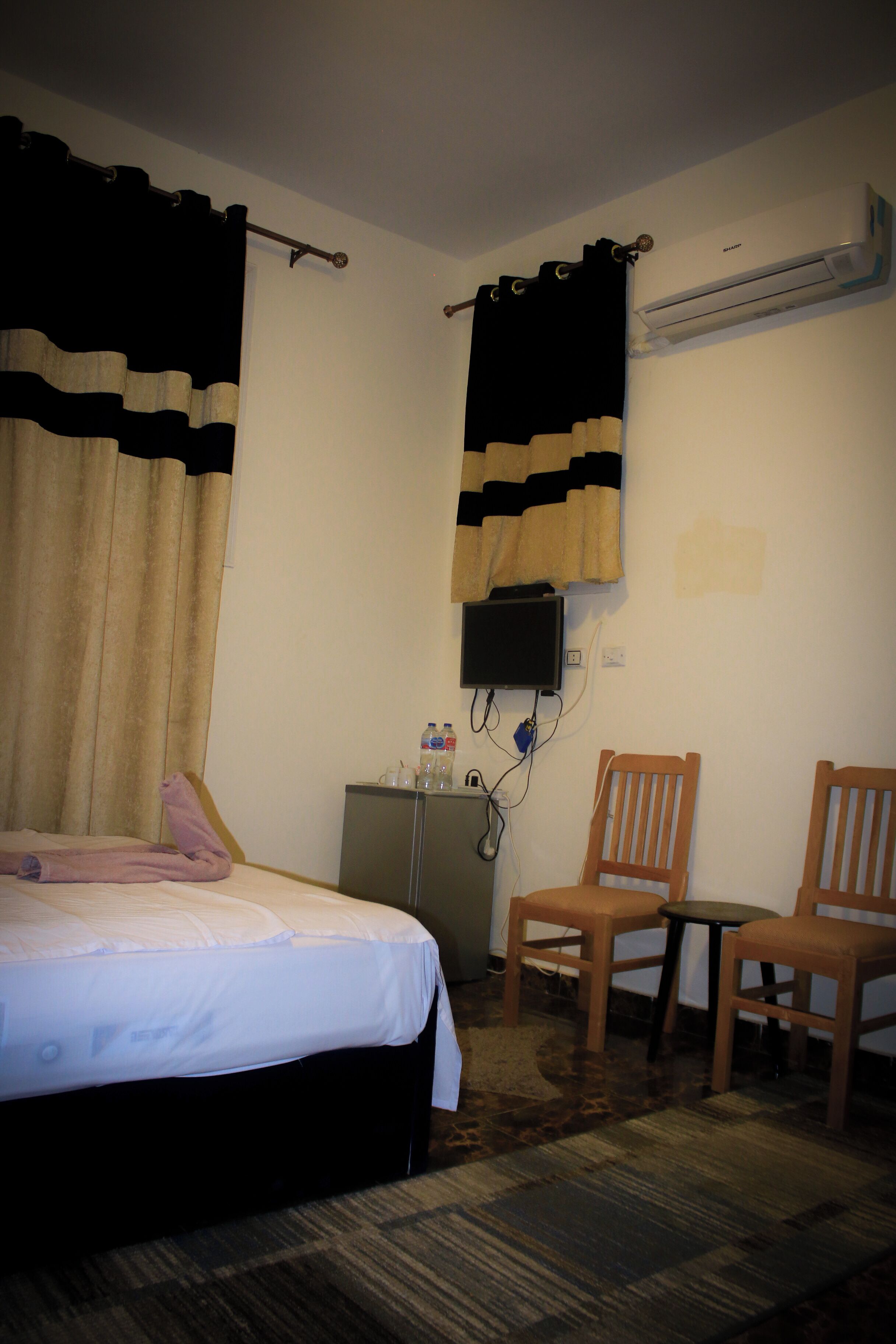 Une chambre d’hôtel comprenant un lit, deux chaises en bois, une petite table, un téléviseur et un appareil de climatisation.