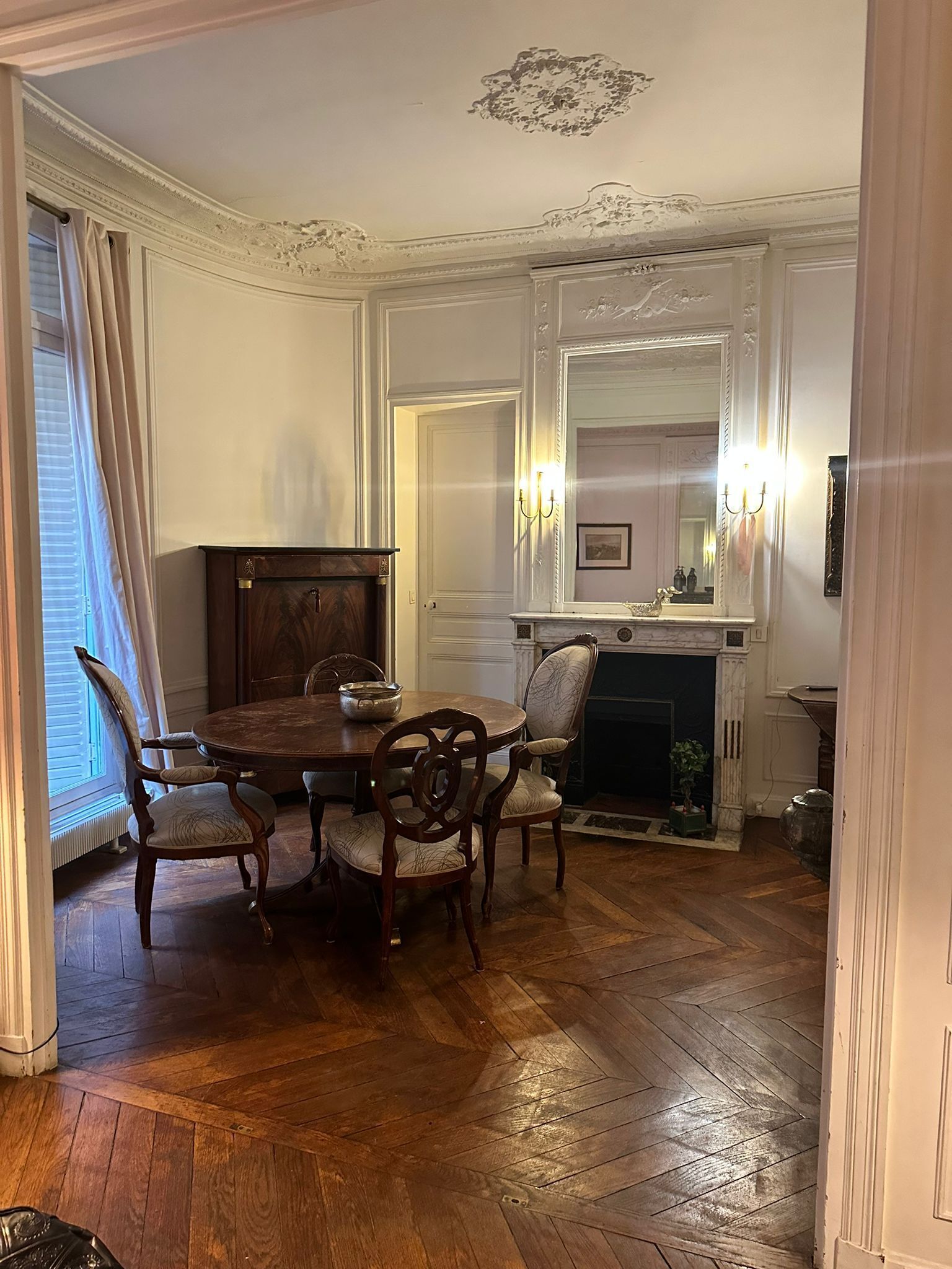 A formal dining room with a wooden table and chairs, a fireplace, and a large mirror above the mantel.