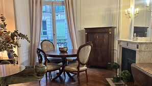 A dining room with a wooden herringbone floor, a round table with four chairs, a fireplace, and a large mirror. - Golden Triangle x Av Montagine & Champs Elysees (Paris)