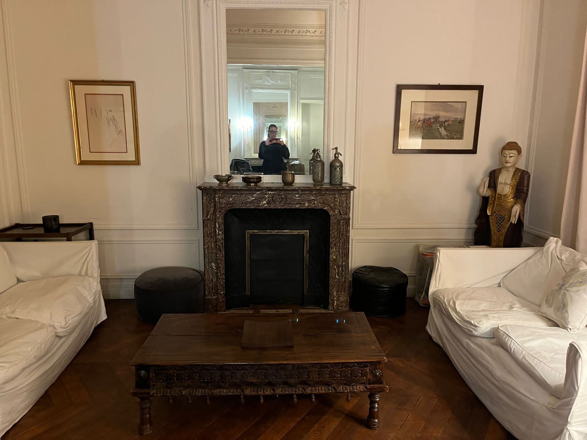 Una habitación con chimenea, dos sofás blancos, una mesa de centro de madera y una estatua de Buda.