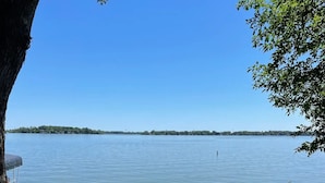 Une vue sur le lac, avec deux fauteuils Adirondack placés face à un lac paisible, le tout entouré d’une pelouse verdoyante et d’un grand arbre.