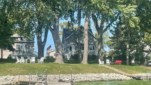 Une propriété au bord du lac, dotée d’un quai, de grands arbres et d’une maison avec une véranda.